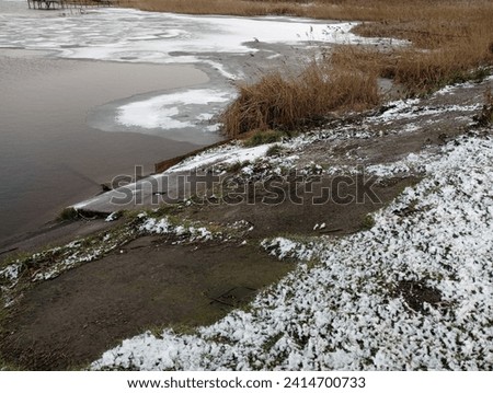 The shore of a frozen winter lake with concrete shores. Winter landscape of a reservoir with the surface part covered with ice.