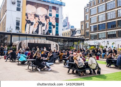 Shoreditch, London, England, UK - April 2019: Pop Up Outdoor Food Area With People Eating Outiside And Big Mural Street Art Celebrating Andy Warhol At The Old Truman Brewery, Ely's Yard, Shoreditch