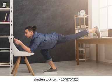 Short Break For Yoga In Office. Flexible Man Practicing Yoga At Workplace, Making Stretching Exercise While Using Tablet, Copy Space. Active Employee At Work, Healthy Lifestyle Concept