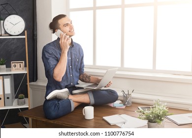 Short Break For Yoga In Office. Flexible Man Practicing Yoga At Workplace, Sitting On Desk In Lotus Pose And Having Coffee With Laptop, Copy Space. Active Employee At Work, Healthy Lifestyle Concept