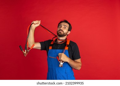 Short circuit. Funny young bearded man, male auto mechanic or fitter wearing blue work dungarees isolated over red studio background. Concept of funny meme emotions, ad, job, insipation, ideas, sales
