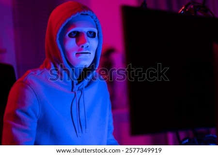 Short of computer hacker wearing white mask stealing data from a laptop. Masked hacker using laptop computer for organizing massive data breach attack on corporate servers in neon room.