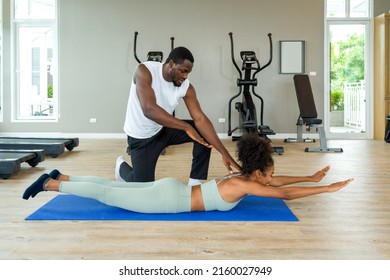 Short Curly Black Hair Coach With Moustache And Beard Teach Young Woman In Sportswear How To Do The Superman Exercise. Helps Reduce Back Pain.