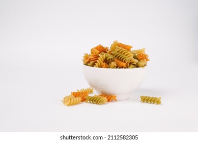 Short, extruded, twisted colored pasta on white background with copy space. Three Colors Rotini or Fusilli Pasta in white bowl and scattered on surface - Powered by Shutterstock