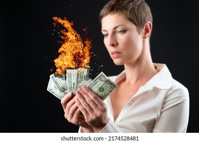 Short haired woman in white business shirt holding burning us dollar banknotes in both hands. Isolated on black background. Concept for crisis, market crash, growing inflation, bear market, recession - Shutterstock ID 2174528481