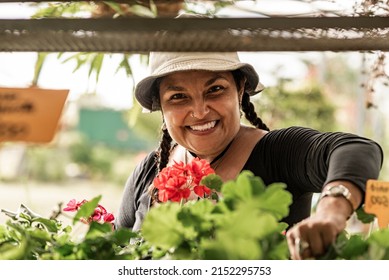 Short, Heavy-set Latina Woman Working In Her Botanical Garden With A Hat On Her Head, Very Happy.