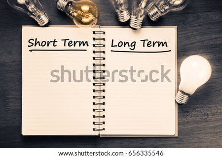 Short term and Long term on opened notebook with glowing light bulb