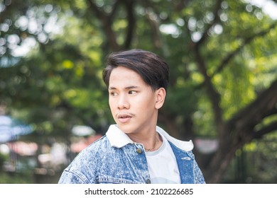 A Short Young Man In A Denim Jacket Looking Away From The Camera. Standing At The Park.