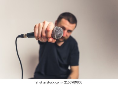 Short-haired Caucasian Bearded Man Holding Microphone In Hand To The Camera, Foreground Focus. Studio Shot Over Gray Background. High Quality Photo