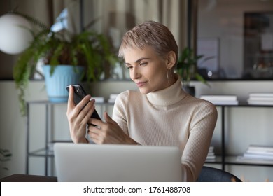 Short-haired confident employee work hold smart phone use agenda planning business meetings with clients sit at workplace desk in front of pc. Busy fruitful workday, independent businesswoman portrait