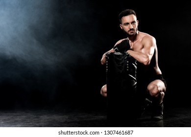 shortless man sitting and holding punching bag on black with smoke - Shutterstock ID 1307461687