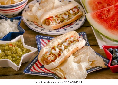 Shot From Above 4th Of July Celebration Picnic Table With Hot Dogs, Chips, Watermelon And Lemonade Sitting On Red, White And Blue Dishes