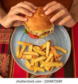 Shot From Above Of A Man's Hands Holding A Hamburger.  Quinoa Veggie Burger Meal Platter With Fries.