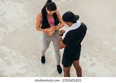 Shot from above on two athletes checking their smartwatch after training. Fitness couple adjusting fitness trackers. - Powered by Shutterstock