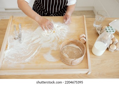 Shot From Above Overhead. Woman's Hans Kneading Dough On Wooden Surface Using Sieve Spoon And Knife. Kitchen Ingredients Eggs Milk Water Baking Cooking Preparing Dough For Pizza Pasta Cookies.