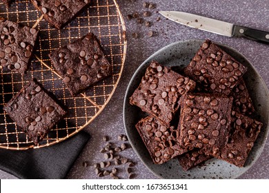 Shot from above stack of keto chocolate chip brownies on gray stoneware plate with additional brownies on copper baking rack with knife on the side