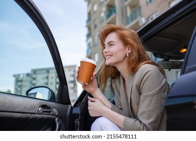 Shot Of Adult Woman Sitting In Her Car With Open Door, Contemplating And Sipping Coffee From A Travel Mug.