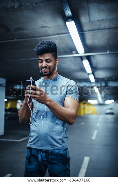 Shot of african\
american athlete man using mobile phone and listening to the music\
in the underground car\
parking.