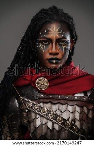 Shot of african woman warrior dressed in red cloak and steel armor isolated on gray background.