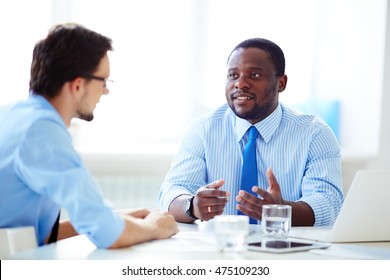 Shot of African-American businessman in shirt and necktie discussing work with Caucasian colleague in shirt and glasses in office. - Shutterstock ID 475109230