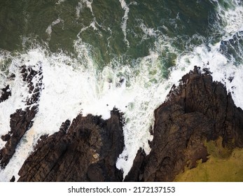 Shot From The Air. Hilly, Overgrown With Green Moss, Ocean Shore. Water Surface With White Foamy Waves. Nature, Geology, Botany, Ecologically Clean Place, Weather. There Are No People In The Photo.