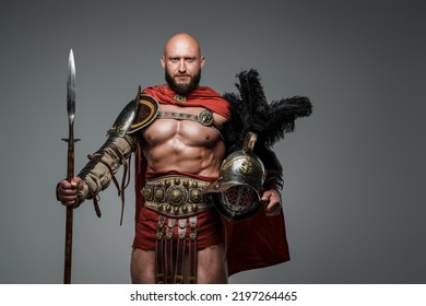 Shot Of Antique Roman Warrior With Muscular Build Holding Helmet And Spear.