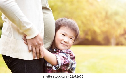 A shot of an Asian boy kissing the belly of his pregnant mother