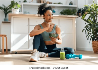 Shot of athletic woman eating a healthy fruit bowl while sitting on floor in the kitchen at home - Powered by Shutterstock