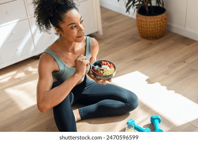 Shot of athletic woman eating a healthy fruit bowl while sitting on floor in the kitchen at home - Powered by Shutterstock