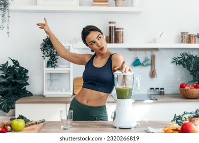 Shot of athletic woman preparing smothie while singing, dancing and listening music with earphones in the kitchen at home. - Powered by Shutterstock