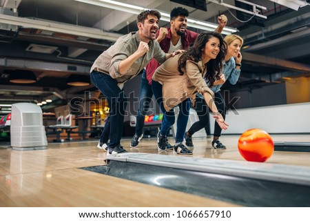 Shot of an attractive brunette throwing the bowling ball while her friends are cheering