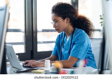 Shot of attractive young afro female doctor talking working with her computer in the consultation.