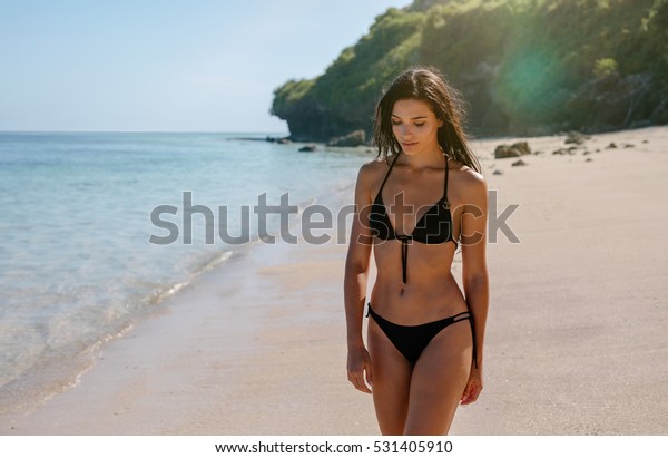 ビキニの魅力的な若い女性が浜辺を歩いている写真 海岸線を歩く女性のモデル の写真素材 今すぐ編集