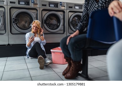 Shot of an attractive young woman listening music by the phone while washing her laundry at laundromat - Powered by Shutterstock