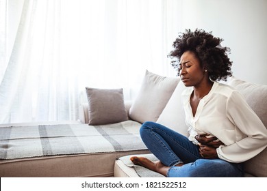 Shot of an attractive young woman suffering from stomach cramps at home. Young woman suffering from strong abdominal pain while sitting on sofa at home