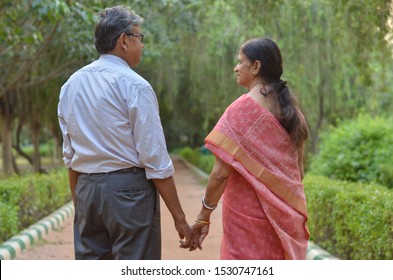 Shot from the back happy looking retired senior Indian man and woman couple smiling and posing in a park holding hands in an outdoor setting in New Delhi, India. Concept love