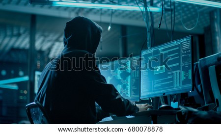 Shot from the Back to Hooded Hacker Breaking into Corporate Data Servers from His Underground Hideout. Place Has Dark Atmosphere, Multiple Displays, Cables Everywhere.