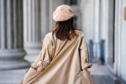 A Shot Of The Back Of A Stylish Chinese Asian Woman In An Elegant French-inspired Outfit (with A Khaki Trench Coat And Beret) In The Corridor Of A Trendy Building During The Day.