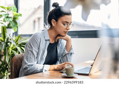 Shot of beautiful attractive entrepreneur woman working with laptop while drinking coffee in the living room at home.