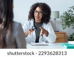 Shot of beautiful cheerful female doctor talking while explaining medical treatment to patient in the consultation.