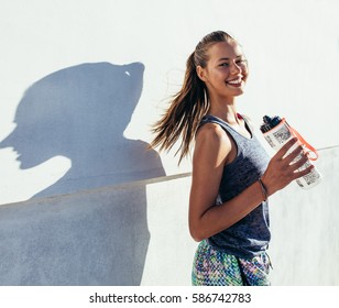 Выстрел красивой женщины-бегуна, стоящей на улице с бутылкой с водой. Фитнес-женщина делает перерыв после тренировки.