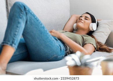Shot of beautiful kind woman relaxing while listening music with headphones lying on couch at home