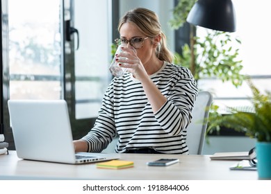 Shot of beautiful mature business woman working with a laptop while drinking glass of water on a desk in the office at home. - Shutterstock ID 1918844006