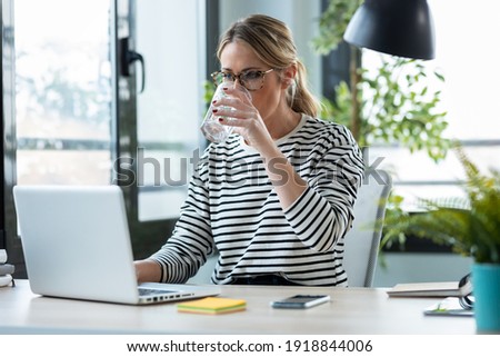 Shot of beautiful mature business woman working with a laptop while drinking glass of water on a desk in the office at home.