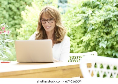 Shot Of A Beautiful Middle Aged Woman Using Laptop While Sitting In The Garden At Home. 