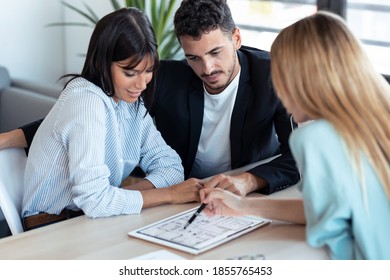 Shot of beautiful real-estate agent showing house plans on electronic tablet while talking to the couple about buying the house in the office. - Shutterstock ID 1855765453