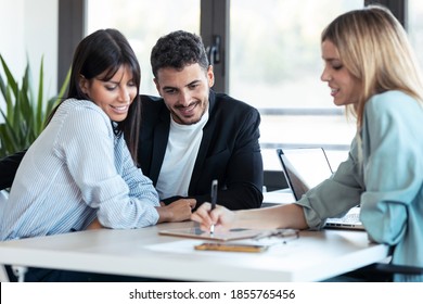 Shot of beautiful real-estate agent showing house plans on electronic tablet while talking to the couple about buying the house in the office. - Shutterstock ID 1855765456