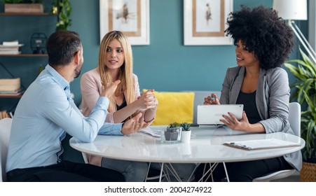 Shot of beautiful real-estate agent showing house plans on electronic tablet while talking to the couple about buying the house in the office. - Shutterstock ID 2004274922