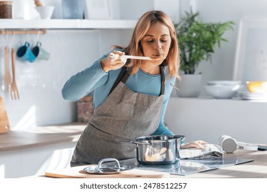 Shot of beautiful woman cooking healthy food in casserole while blowing the spoon to taste the food in the kitchen at home. - Powered by Shutterstock