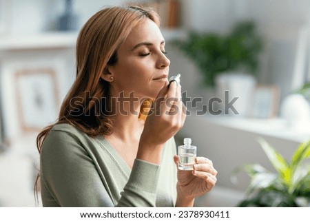 Shot of a beautiful woman holding a bottle of essential oil while testing it sitting on a couch at home.